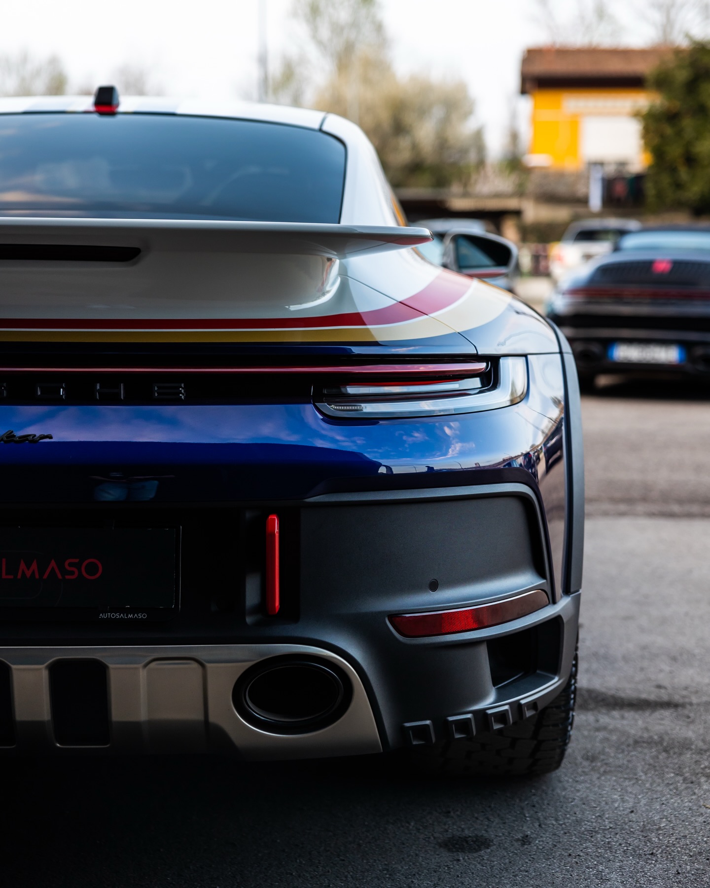 Retro di Porsche bianca e blu con strisce rosse e oro, alettone e paraurti grigio opaco, portatarga AutoSalmaso